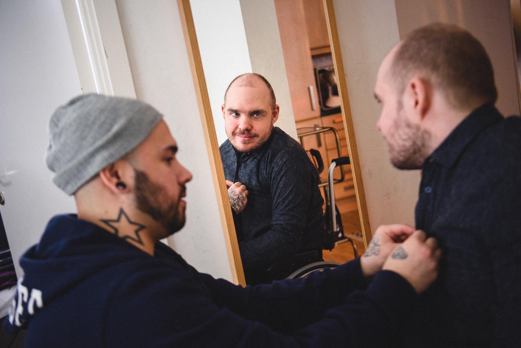 Person i rullstol speglar sig och får hjälp att rätta till skjotan